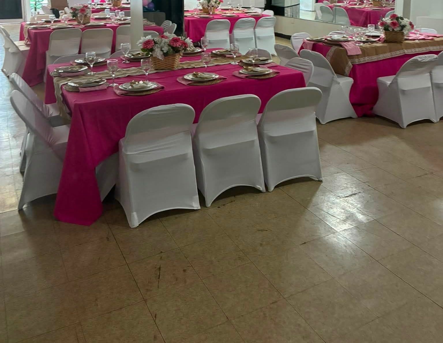 An event hall after cleaning, tables set with pink cloths, white covered chairs and flower centrepieces on a clean tiled floor.