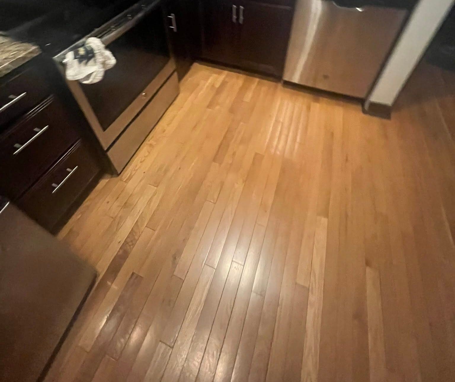A kitchen after cleaning: gleaming hardwood floor, dark wood cabinets and a stainless steel dishwasher and oven.